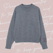 Gray sweater with "Brave, Soft, Strong" embroidered on the sleeve, seen on flat lay - Little Mama Shirt Shop
