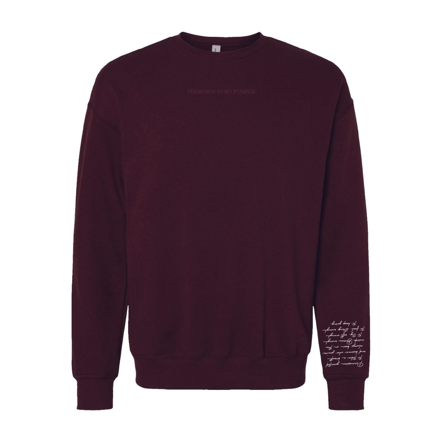 Maroon crewneck with "Permission To Be Optimistic" on chest and permission to be paragraph printed on sleeve, shown on flat lay - Little Mama Shirt Shop