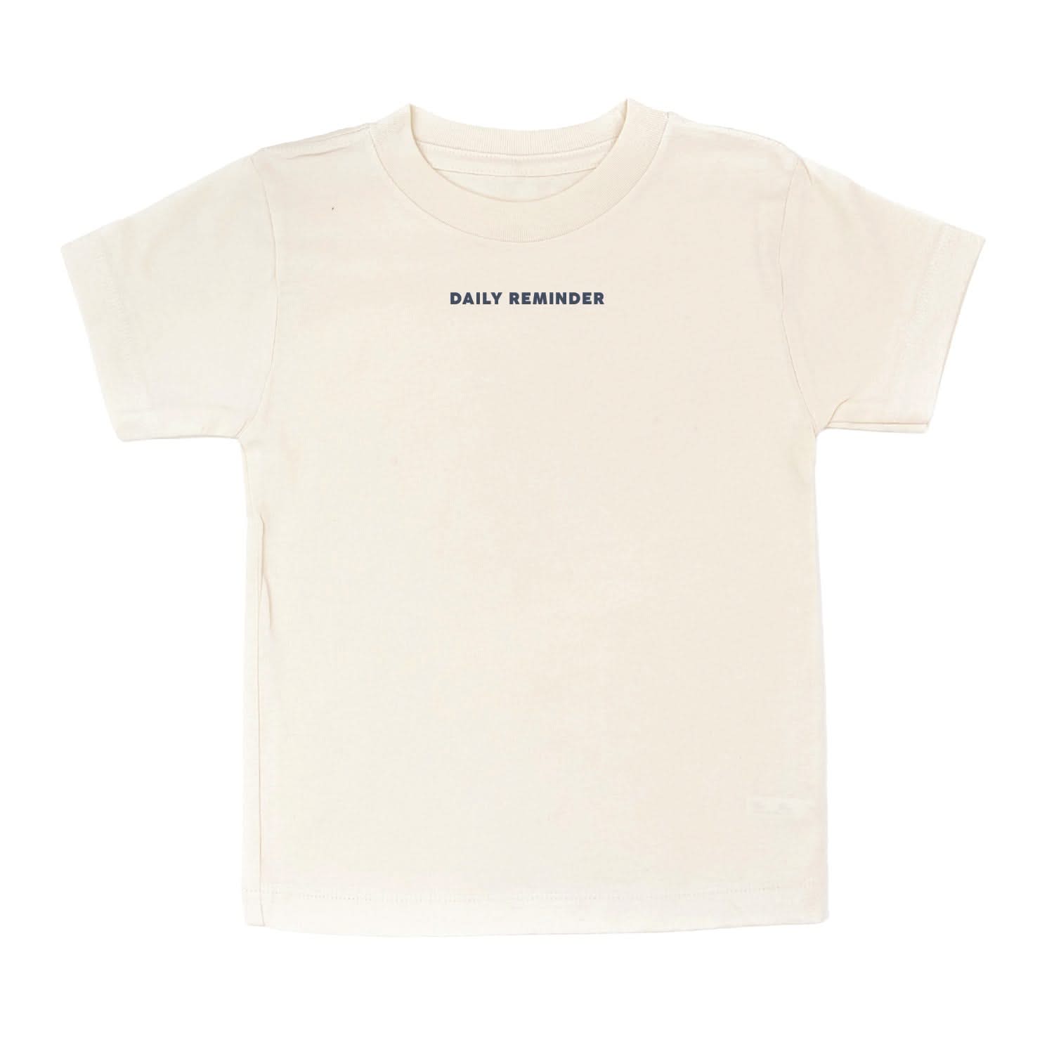 Natural child tee with 'daily reminder' printed on front, seen on flat lay - Little Mama Shirt Shop