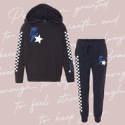 Child black sweater and joggers with checkers pattern on arm and leg, and blue lightning bolt with 'be you' in it flanked by a white star, seen on flat lay - Little Mama Shirt Shop