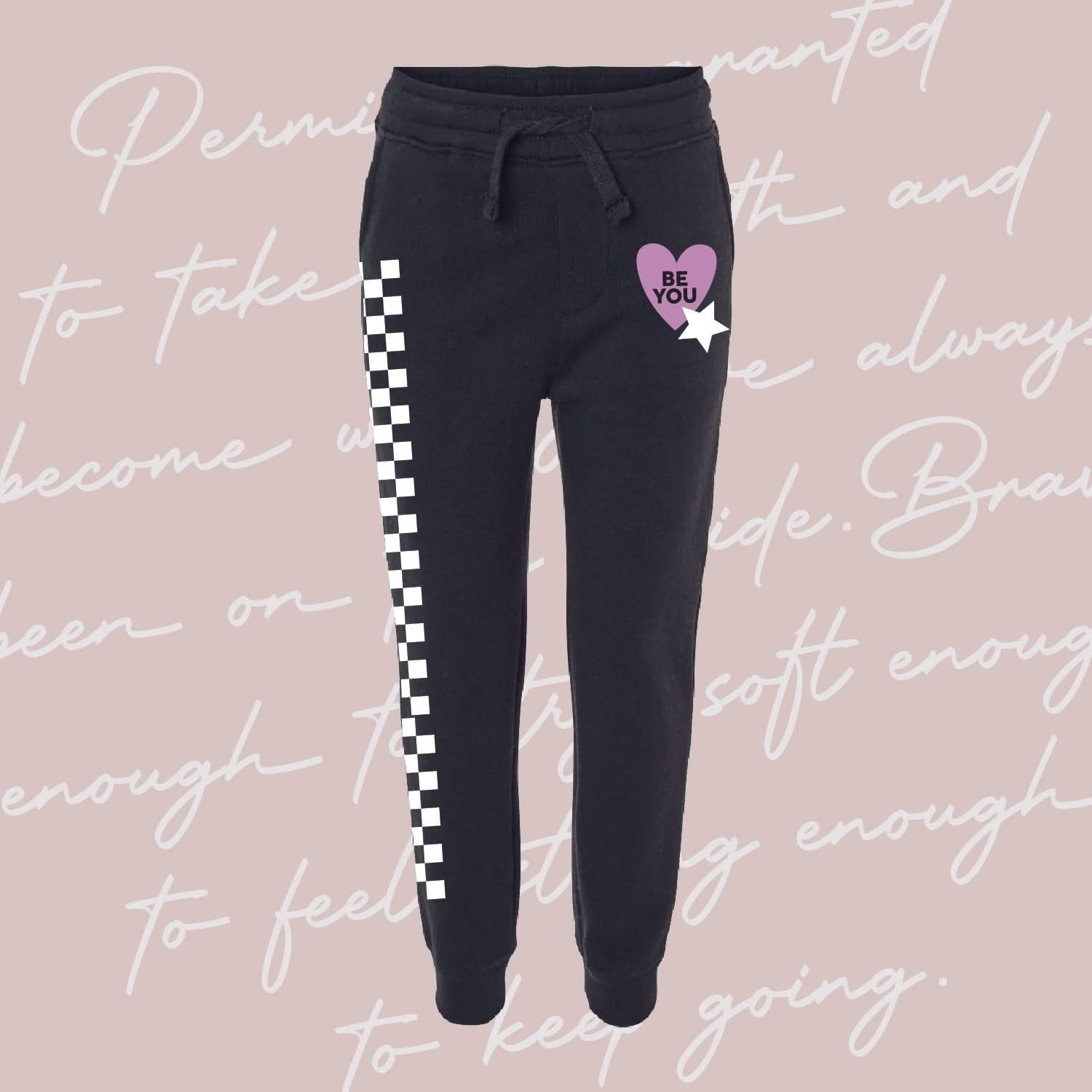 Child black joggers with checkers pattern on leg, and Purple Heart with 'be you' in it flanked by a white star, seen on flat lay - Little Mama Shirt Shop