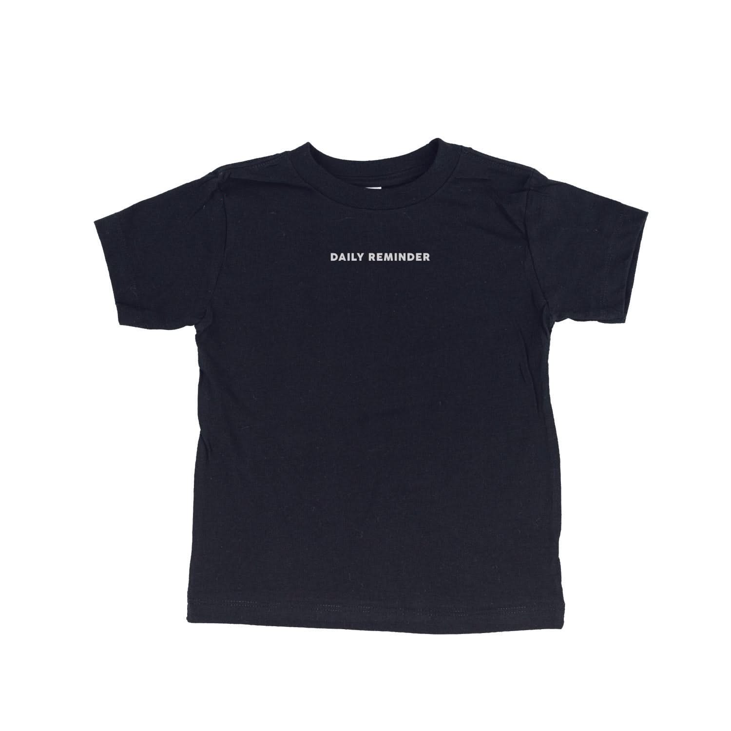 Black child tee with 'daily reminder' printed on front, seen on flat lay - Little Mama Shirt Shop