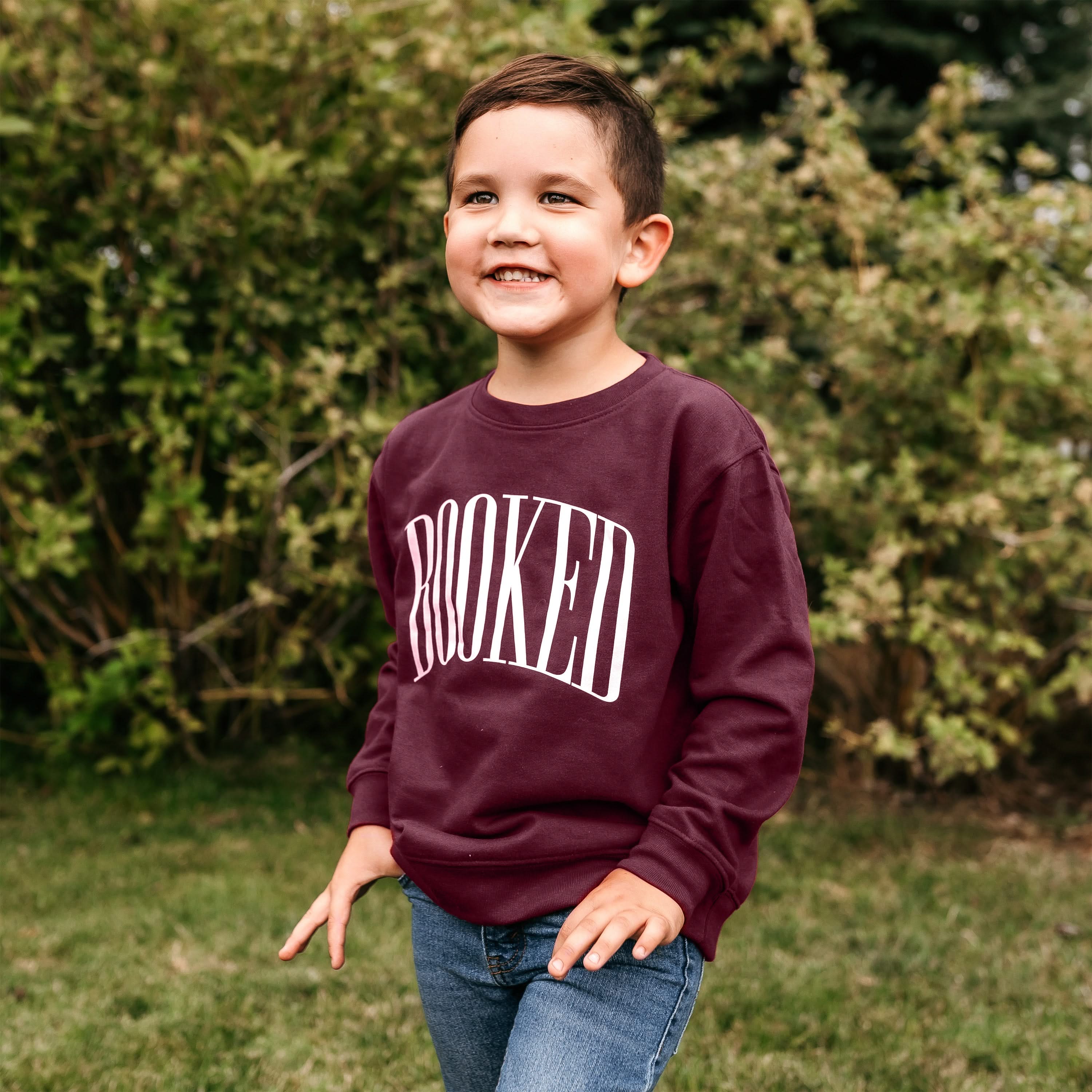 Child sweater in maroon with 'BOOKED' graphic on chest, shown on model – Little Mama Shirt Shop