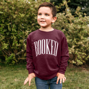 Child sweater in maroon with 'BOOKED' graphic on chest, shown on model – Little Mama Shirt Shop