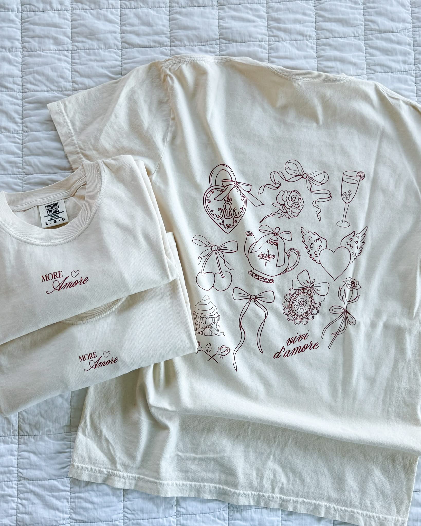 Adult tee in ivory with "More Amore" print on front and Valentines collage design on back, shown on flat lay – Little Mama Shirt Shop