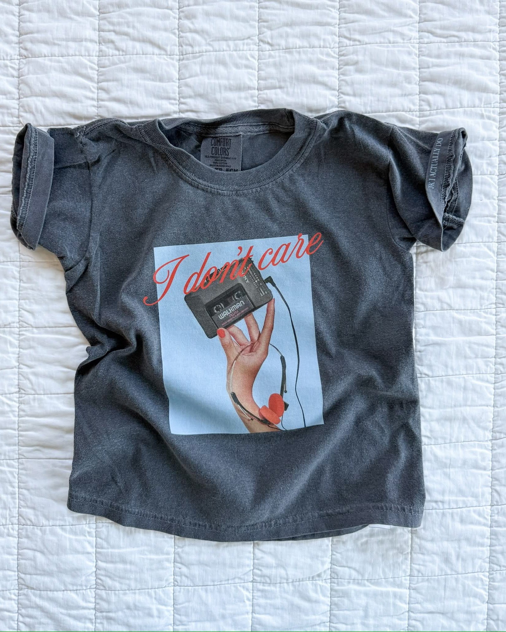 Child tee with "I Don't Care" retro cassette on front and "JK I Actually Do" text on sleeve, shown on flat lay  – Little Mama Shirt Shop