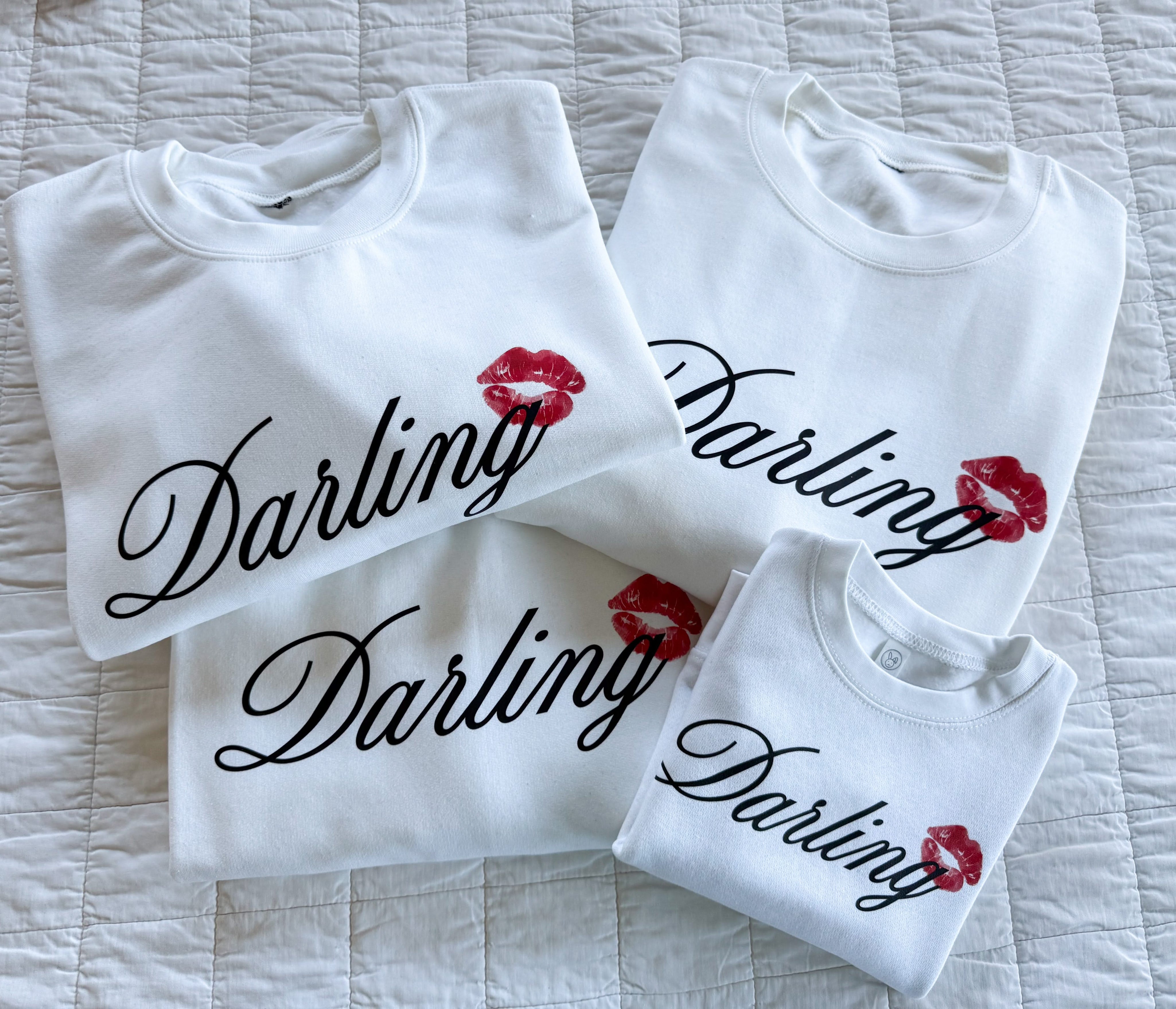 Adult white sweaters with "Darling" script and lipstick kiss design, shown on flat lay  – Little Mama Shirt Shop