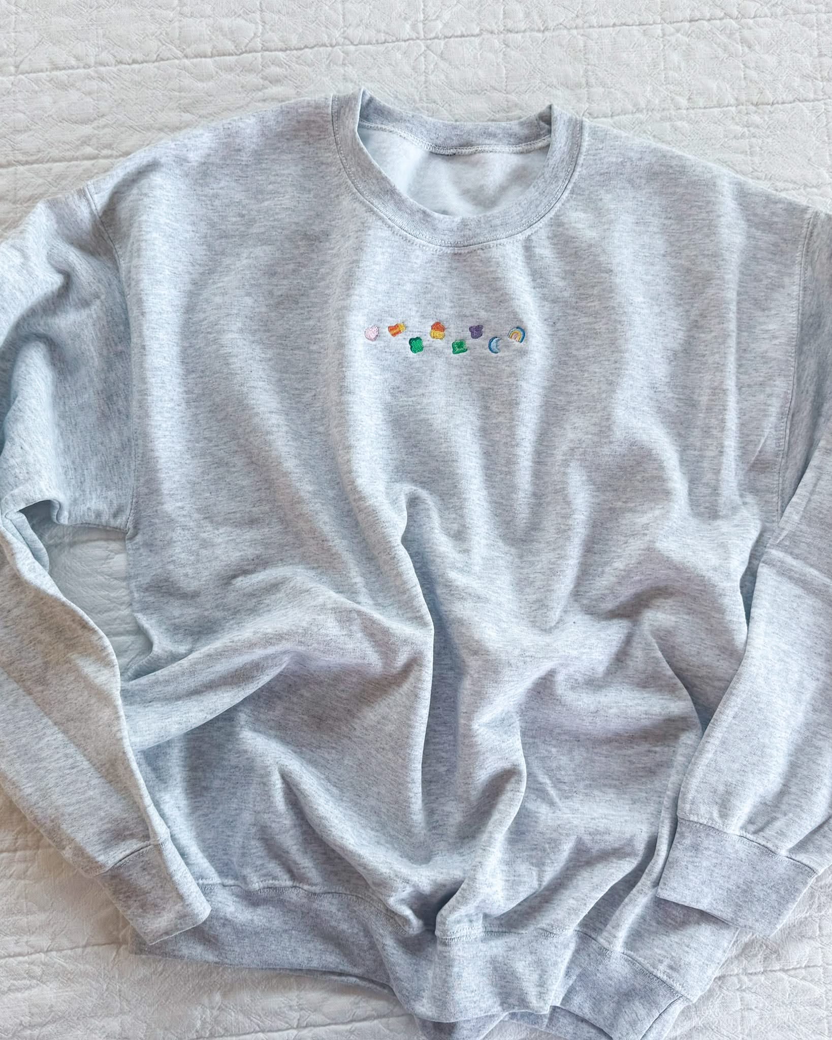 Ash adult basic fleece with lucky charm marshmallows embroidered on chest, seen on flat lay - Little Mama Shirt Shop