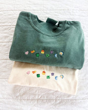 Green and ivory CC tees with lucky charm marshmallows embroidered on chest, seen on flat lay - Little Mama Shirt Shop