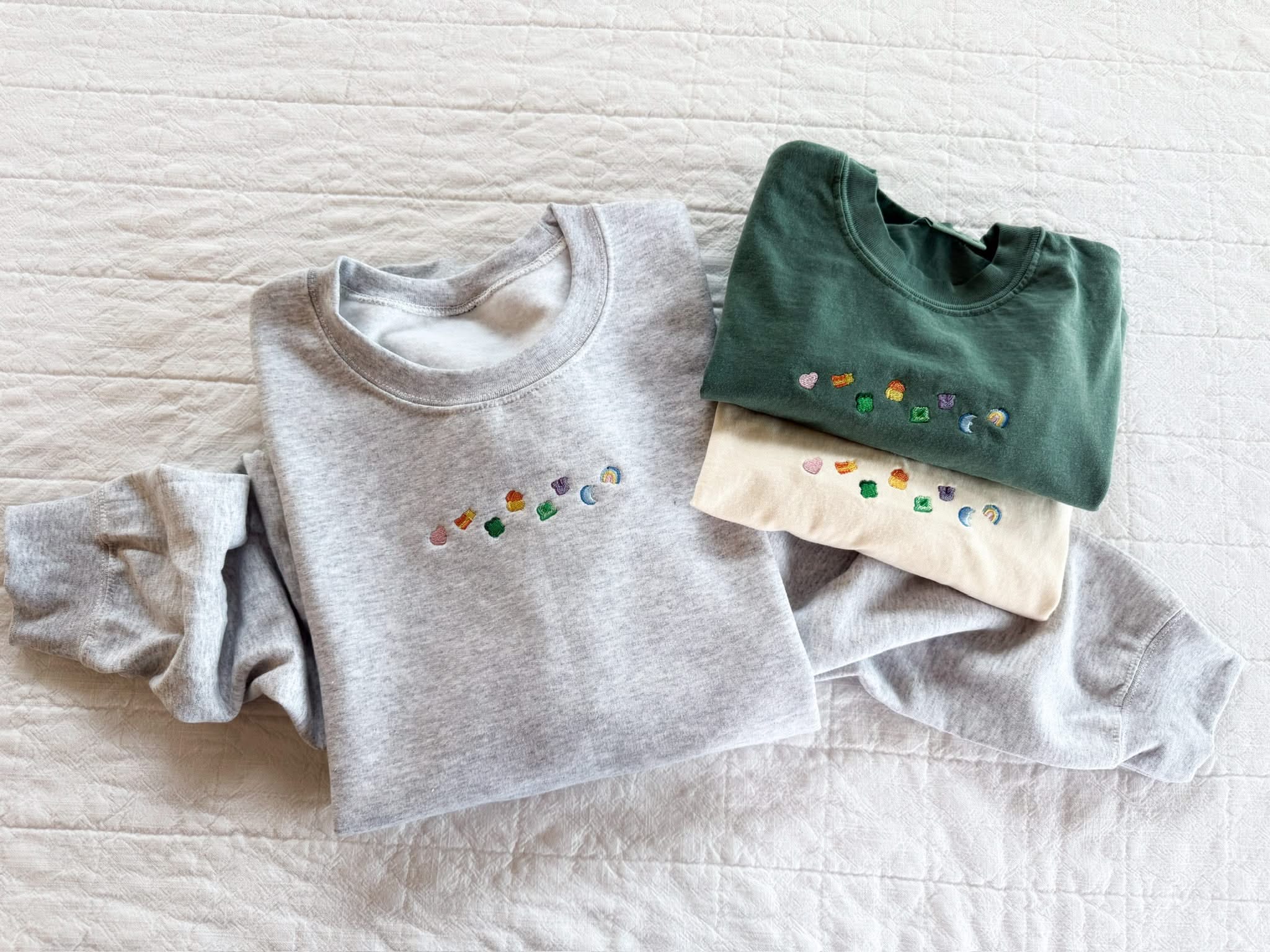 Ash adult basic fleece and green and ivory CC tees with lucky charm marshmallows embroidered on chest, seen on flat lay - Little Mama Shirt Shop
