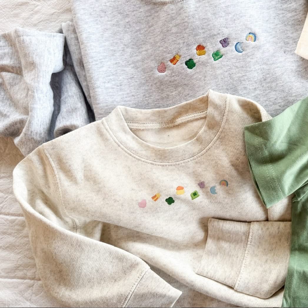 Natural heather child sweater with printed lucky charm marshmallows design on chest, seen on flat lay - Little Mama Shirt Shop