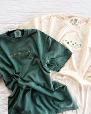Green and ivory CC tees with lucky charm marshmallows embroidered on chest, seen on flat lay - Little Mama Shirt Shop
