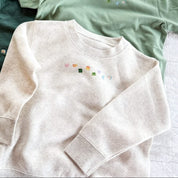Natural heather child sweater with printed lucky charm marshmallows design on chest, seen on flat lay - Little Mama Shirt Shop