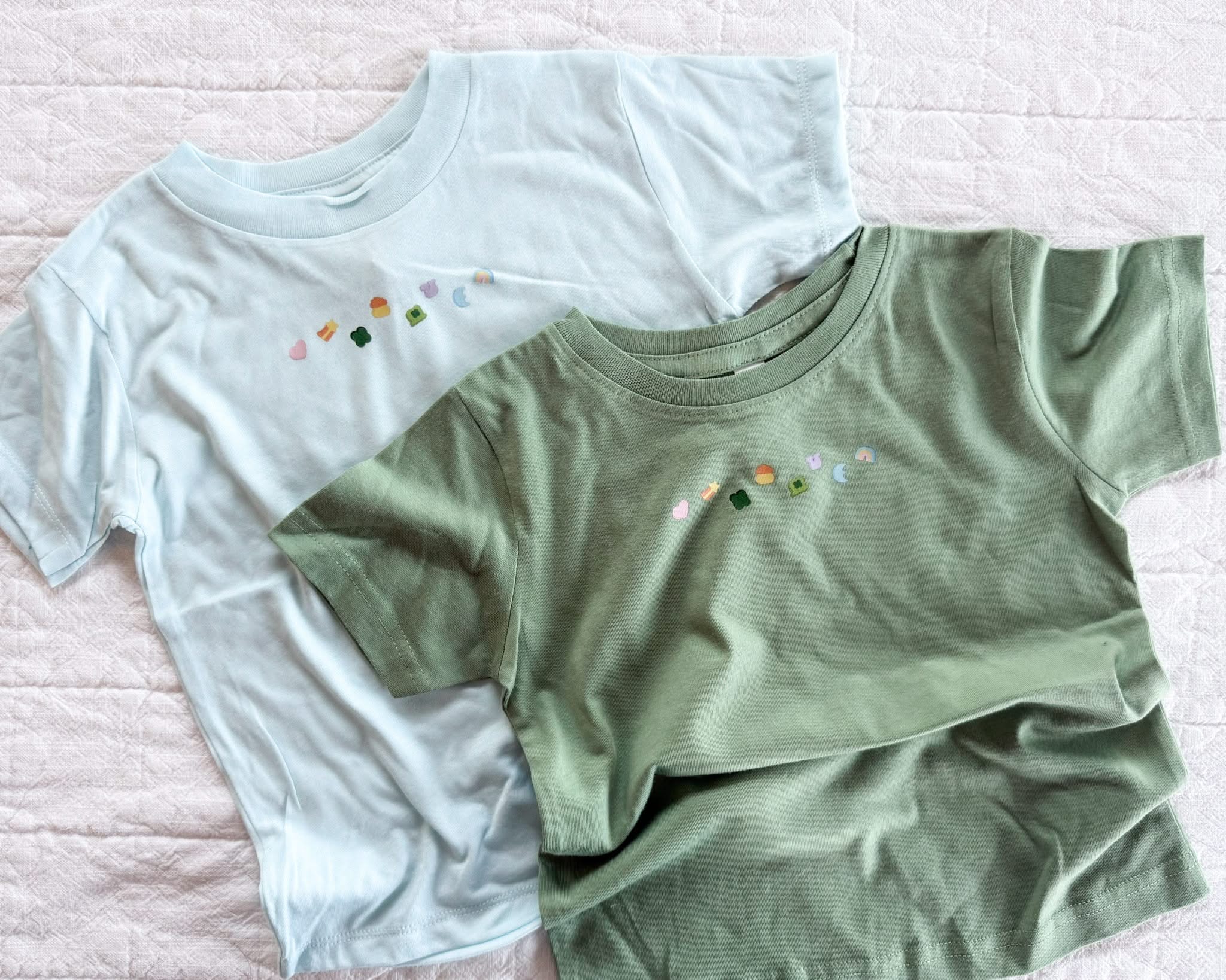 Ice blue and sage child tees with printed lucky charm marshmallows design on chest, seen on flat lay - Little Mama Shirt Shop