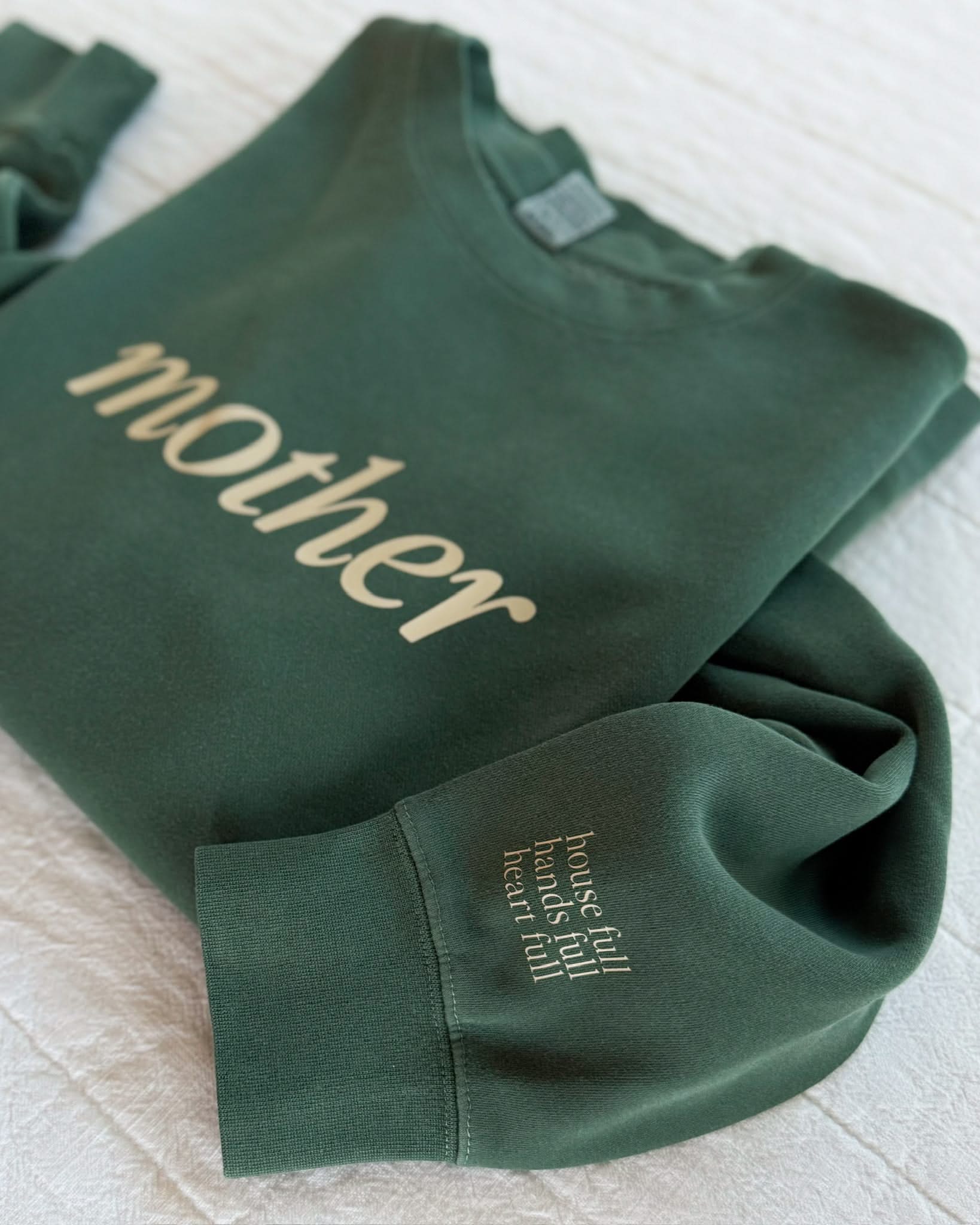 Adult pigment crewneck in alpine with 'mother' printed on the front and 'house full, hands full, heart full' printed on sleeve, seen on flat lay - Little Mama Shirt Shop