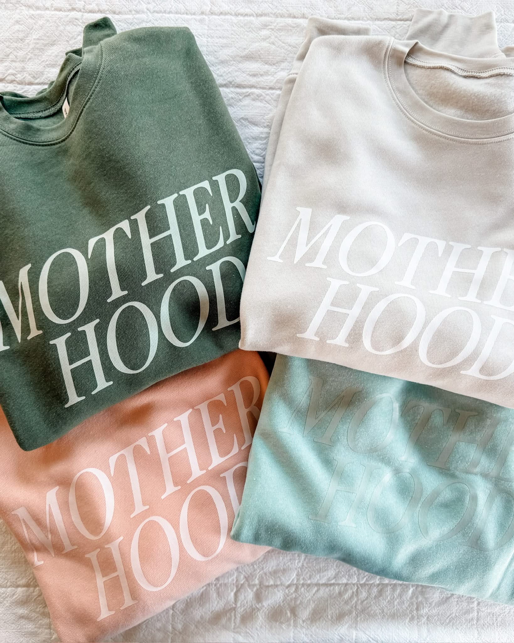 Adult fleece in army green, cream, blush, and mint with 'motherhood' printed on the front in tone on tone, seen on flat lay - Little Mama Shirt Shop