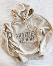 Adult pigment hoodie in cream with 'motherhood' printed on front with floral design behind and 'living the dream' printed on the sleeve, seen on flat lay - Little Mama Shirt Shop