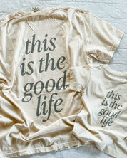 Adult tee in ivory and child tee in cream with 'this is the good life' printed on the back, seen on flat lay - Little Mama Shirt Shop