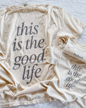 Adult tee in ivory and child tee in cream with 'boyhood' printed on the front and 'this is the good life' printed on the back, seen on flat lay - Little Mama Shirt Shop