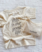 Child tee in cream with 'boyhood' printed on the front and 'this is the good life' printed on the back, seen on flat lay - Little Mama Shirt Shop