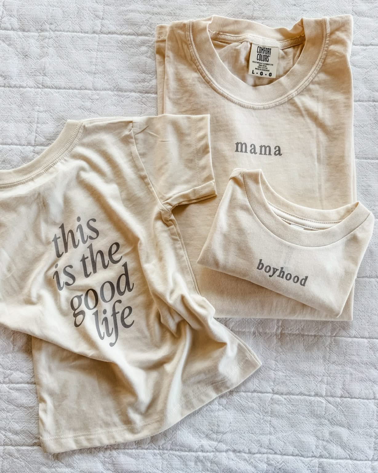Adult tee in ivory and child tee in cream with 'boyhood' and 'mama' printed on the front and 'this is the good life' printed on the back, seen on flat lay - Little Mama Shirt Shop