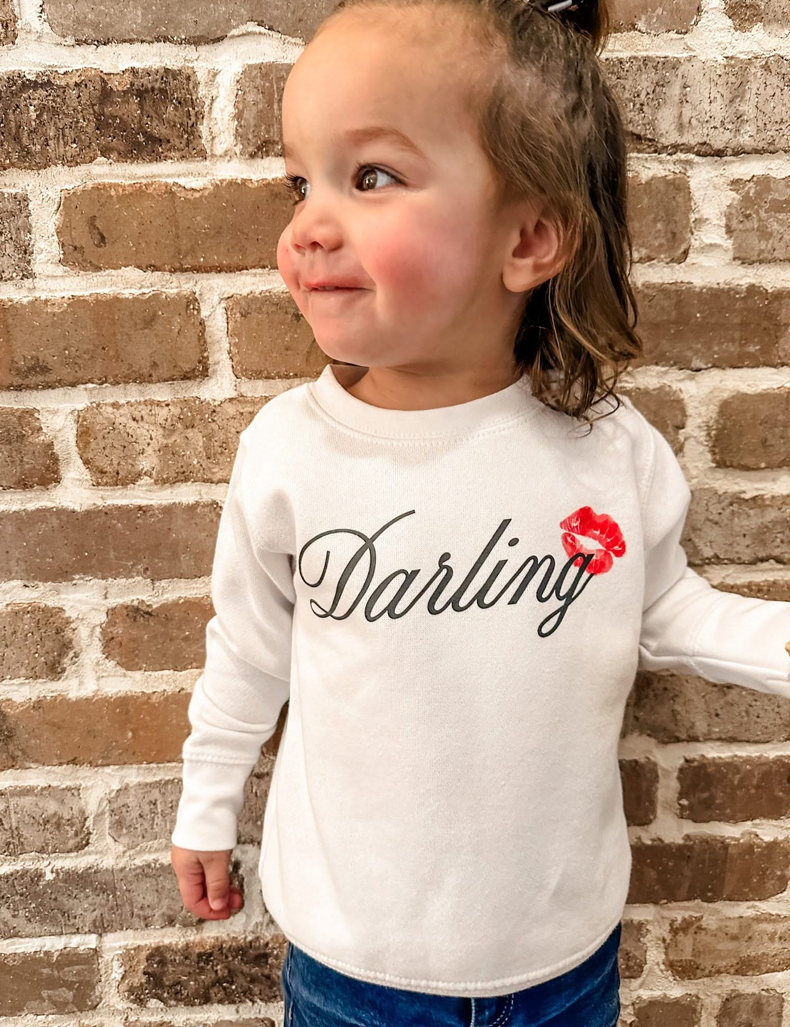 Child white sweater with "Darling" script and lipstick kiss design, shown on model  – Little Mama Shirt Shop