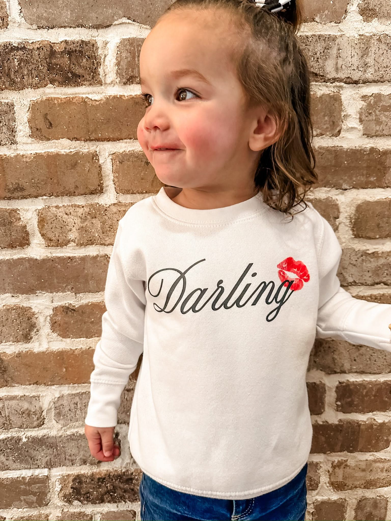 Child white sweater with "Darling" script and lipstick kiss design, shown on model  – Little Mama Shirt Shop