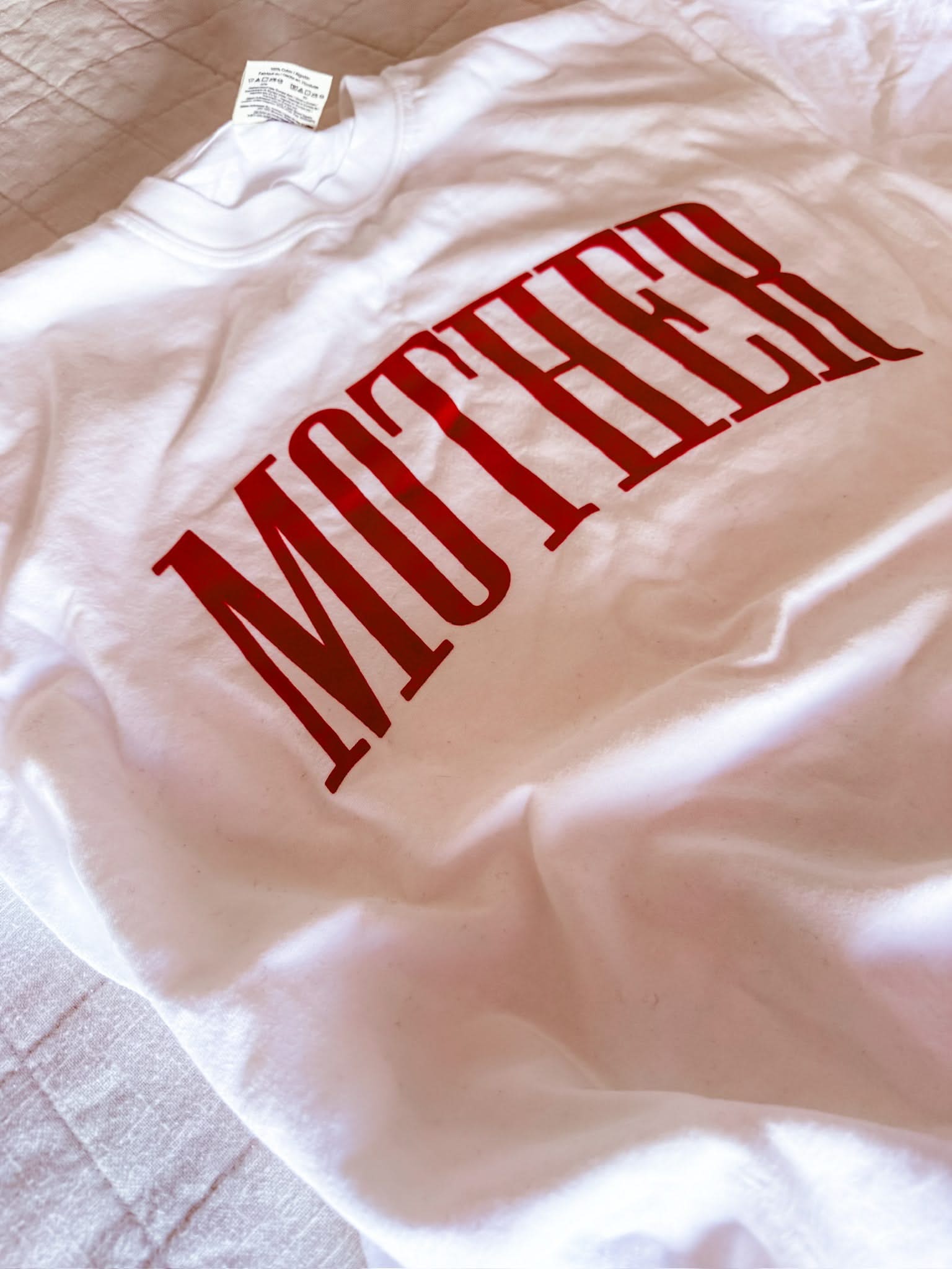 White adult comfort colors tee with red 'mother' puff print across the front, seen on flat lay - Little Mama Shirt Shop