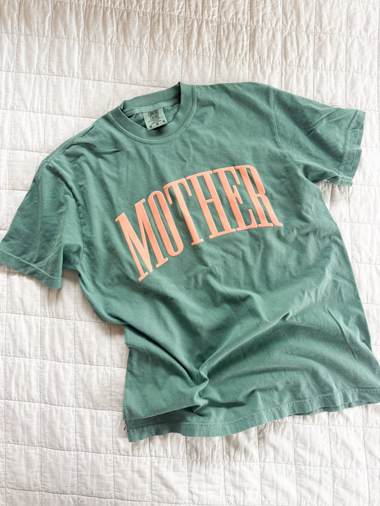 Light green adult comfort colors tee with coral 'mother' puff print across the front, seen on flat lay - Little Mama Shirt Shop