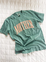 Light green adult comfort colors tee with coral 'mother' puff print across the front, seen on flat lay - Little Mama Shirt Shop