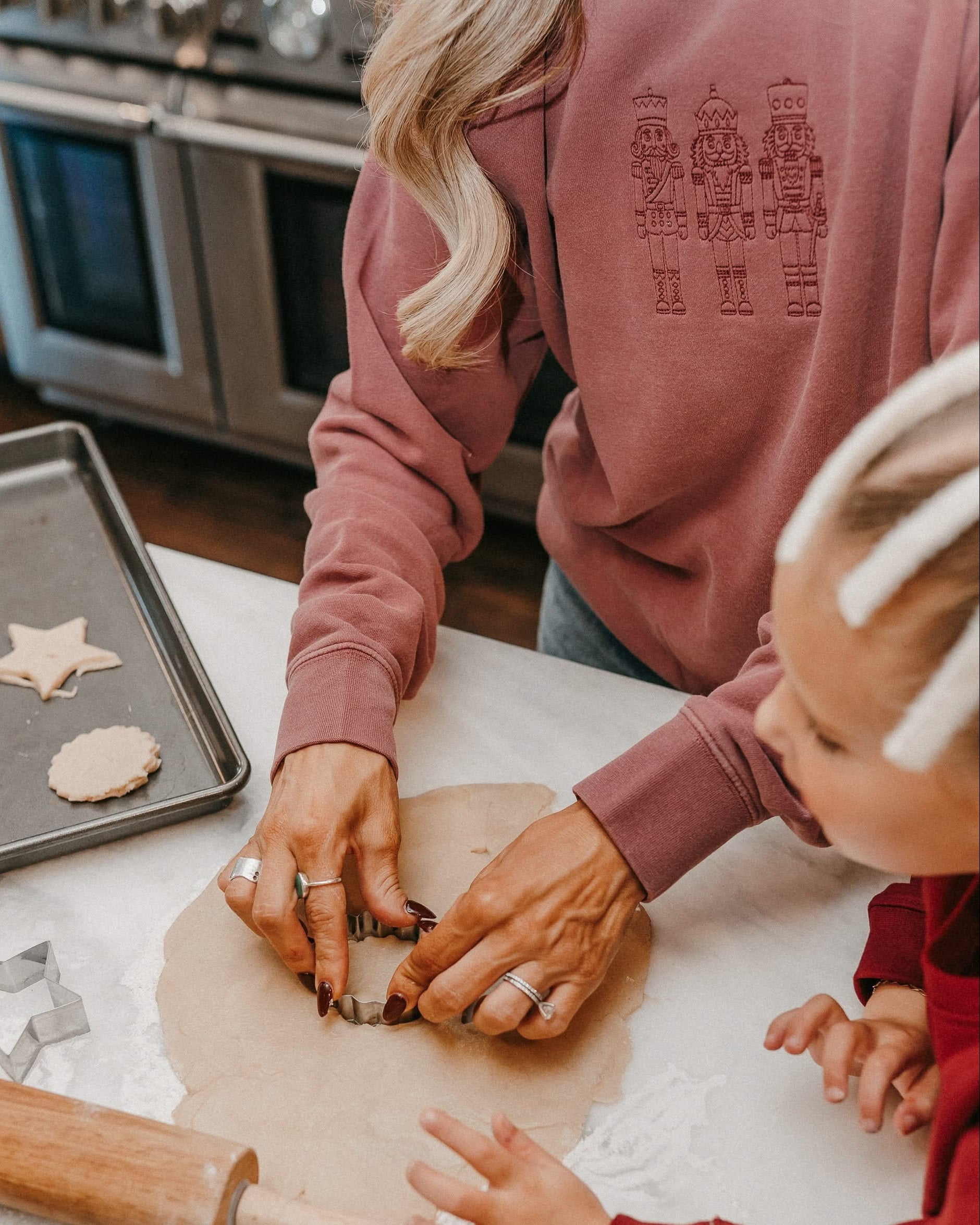 Adult sweater in dusty pink with 3 embroidered nutcrackers on chest, shown on model – Little Mama Shirt Shop