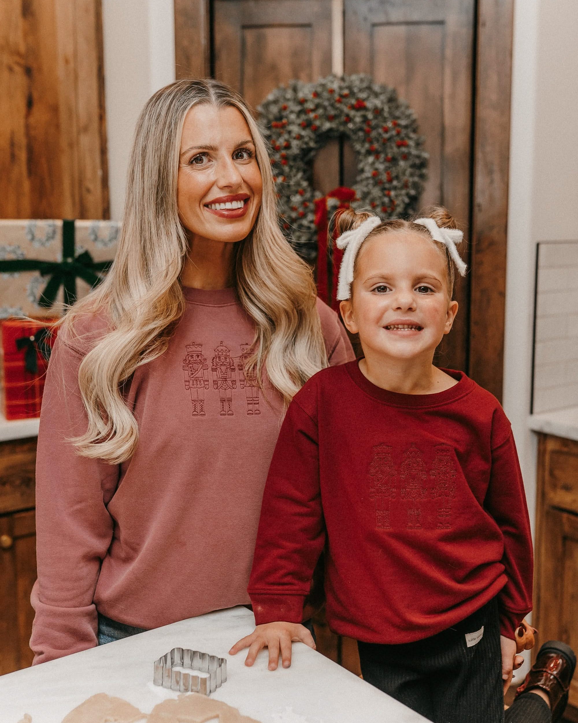 Adult sweater in dusty pink and child sweater in red with 3 embroidered nutcrackers on chest, shown on models – Little Mama Shirt Shop