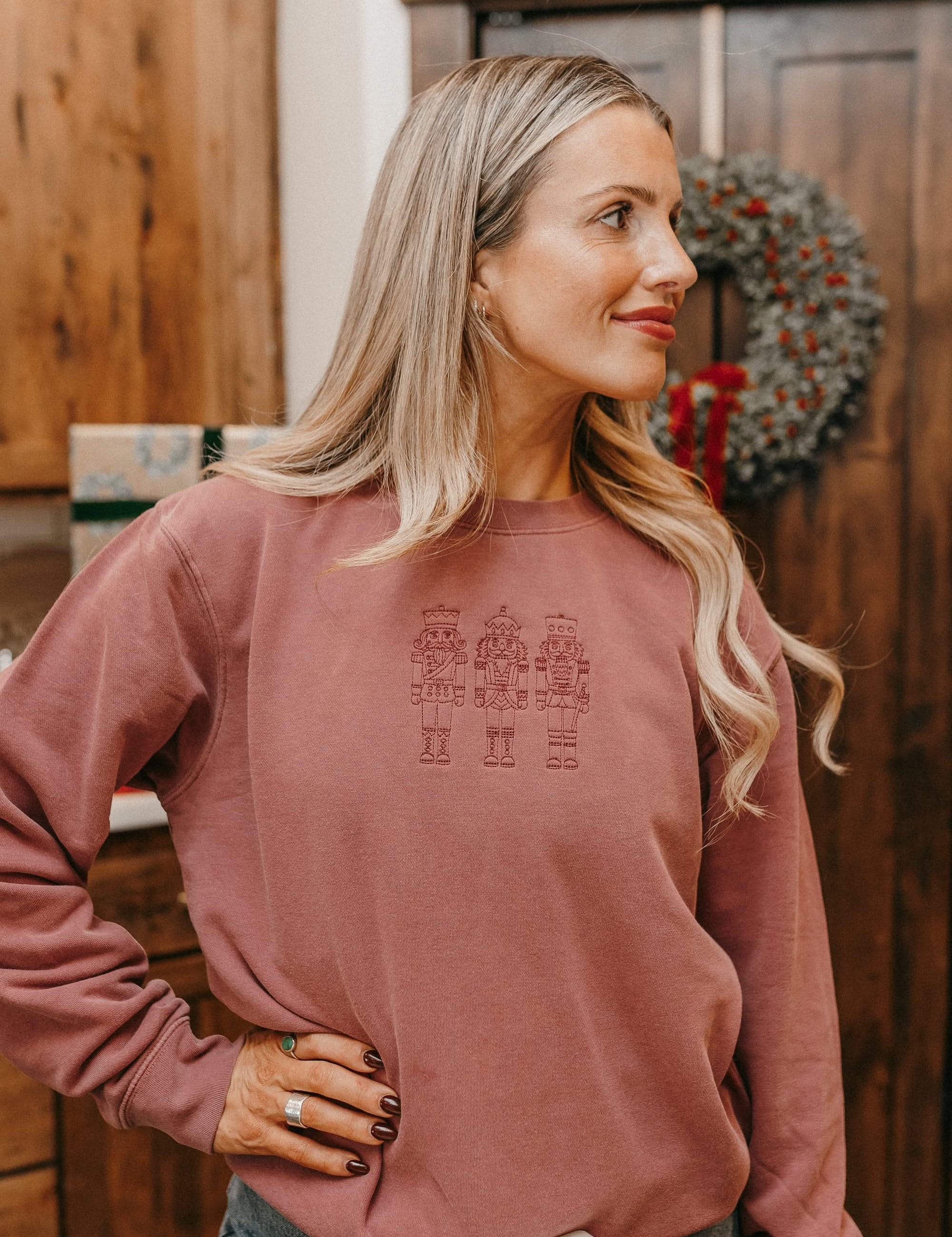 Adult sweater in dusty pink with 3 embroidered nutcrackers on chest, shown on model – Little Mama Shirt Shop