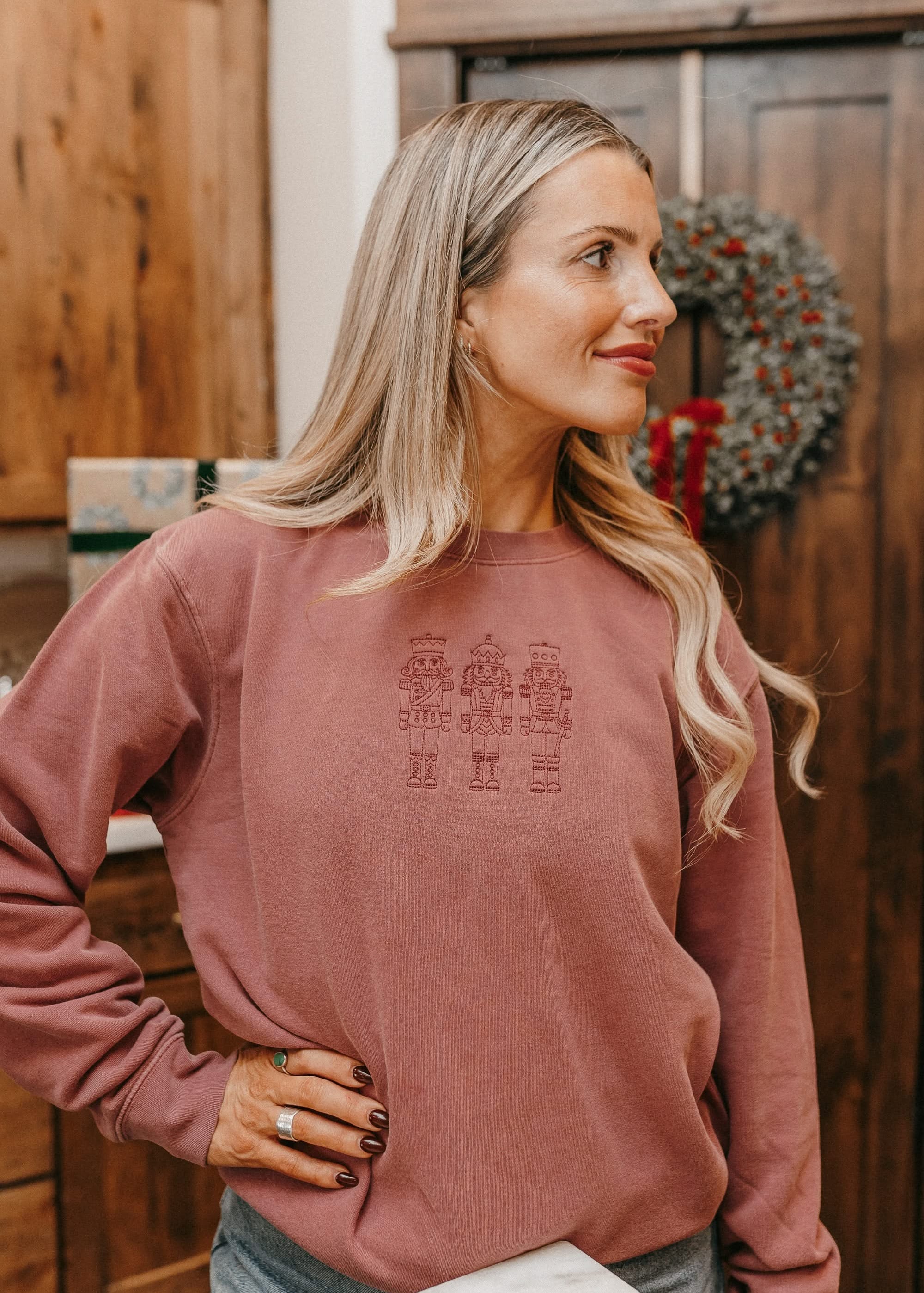 Adult sweater in dusty pink with 3 embroidered nutcrackers on chest, shown on model – Little Mama Shirt Shop