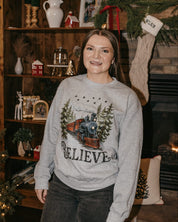 Adult Sweater in gray with winter train and 'Believe' on chest, shown on model – Little Mama Shirt Shop