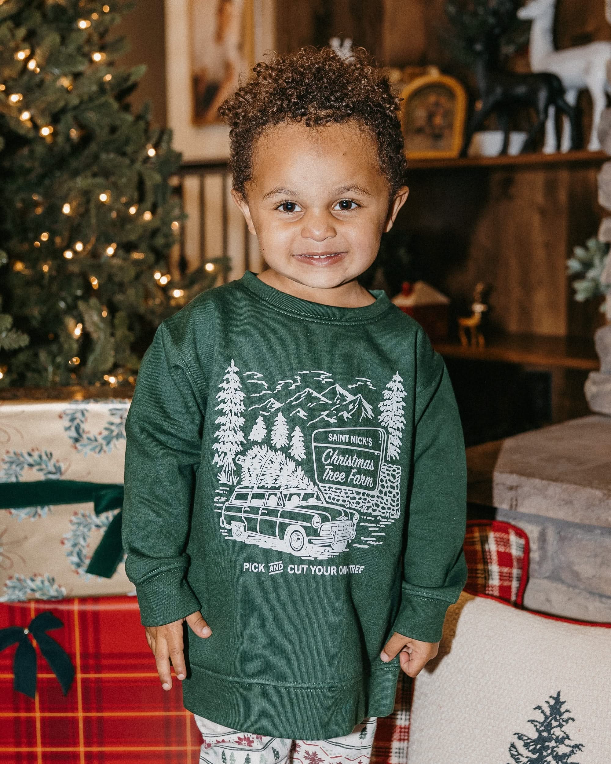 Child sweater in forest with St. Nick's Christmas Tree Farm graphic on the front, shown on model – Little Mama Shirt Shop