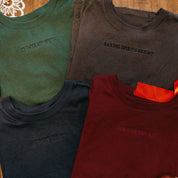 Adult tee in forest, dark gray, navy, and maroon with Christmas messages on front, shown on flat lay – Little Mama Shirt Shop