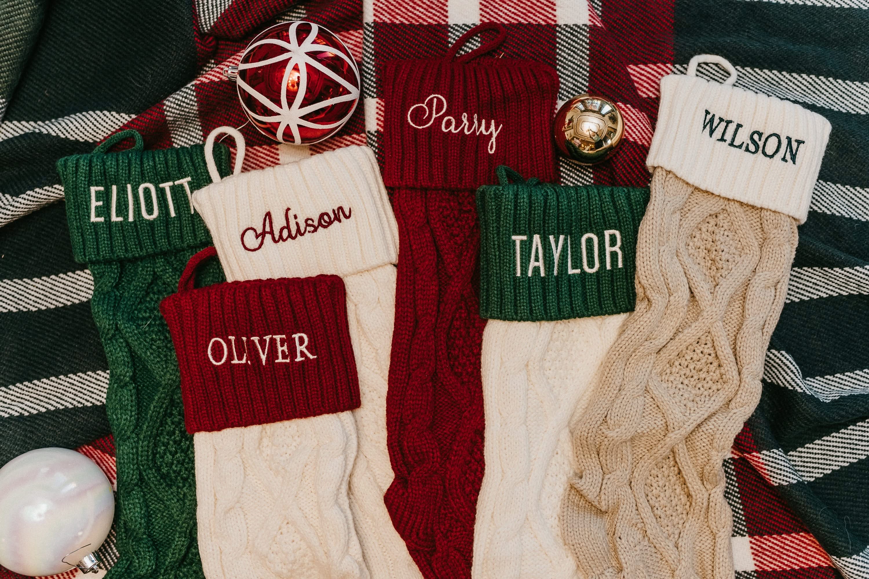 Christmas stocking in tan, cream, red, and green with personalized name printed on cuff, shown on flat lay – Little Mama Shirt Shop