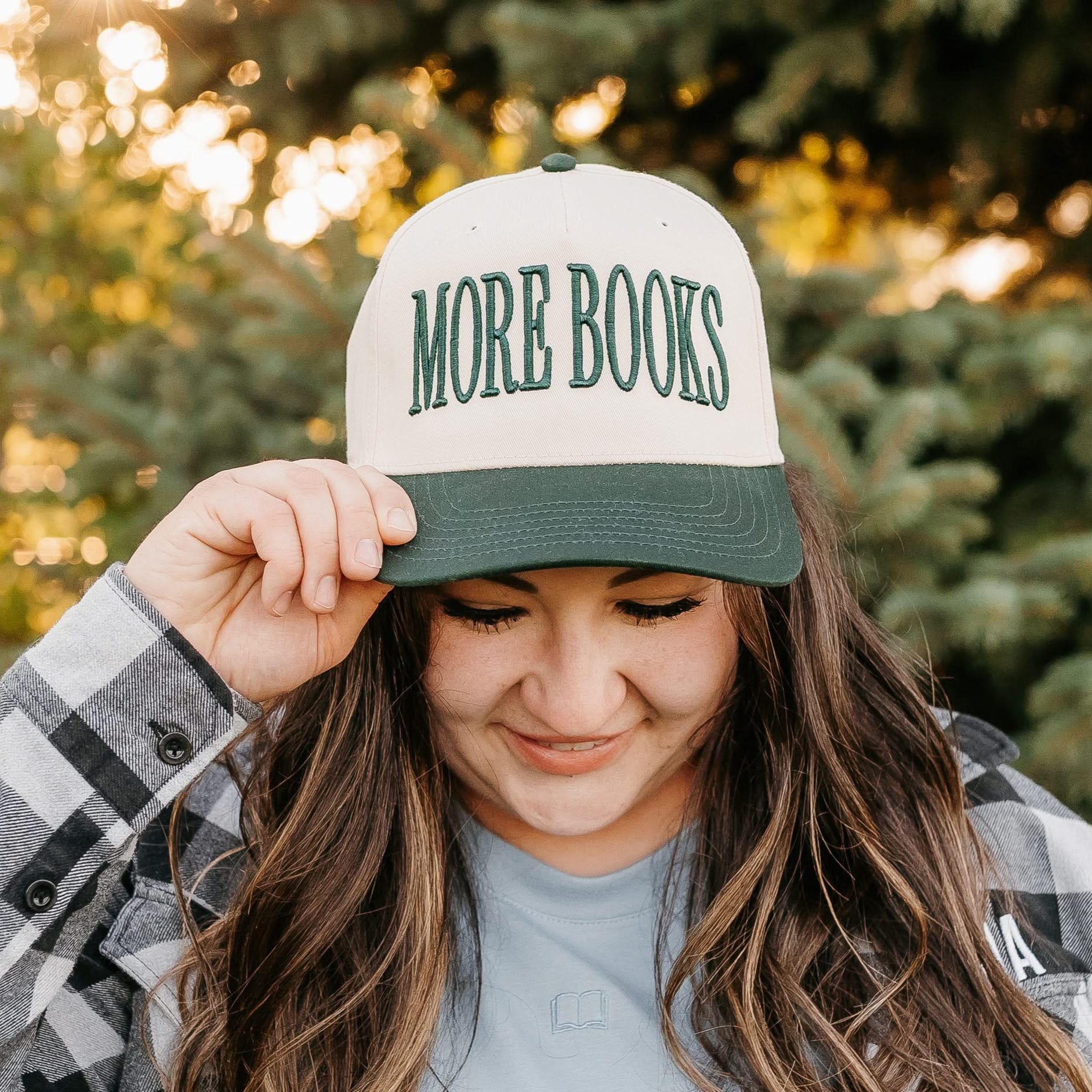 Tan and green trucker hat with adjustable closure, featuring a front embroidered design that reads “More Books" on model - Little Mama Shirt Shop
