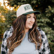 Tan and green trucker hat with adjustable closure, featuring a front embroidered design that reads “More Books" on model - Little Mama Shirt Shop