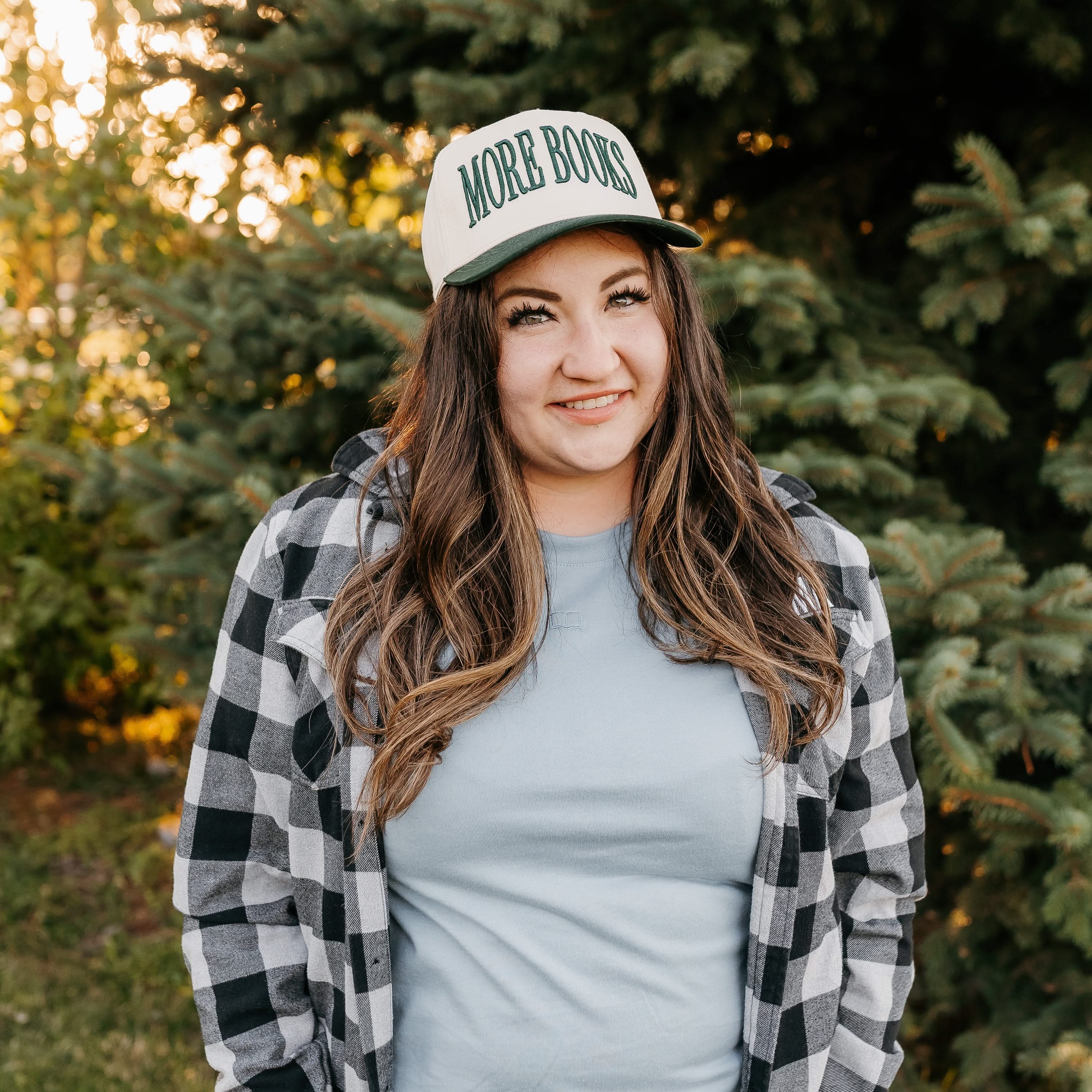 Tan and green trucker hat with adjustable closure, featuring a front embroidered design that reads “More Books" on model - Little Mama Shirt Shop