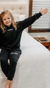 Kids hoodie and jogger in black with white hearts on chest and 'Kid Life' on leg of joggers on model - Little Mama Shirt Shop