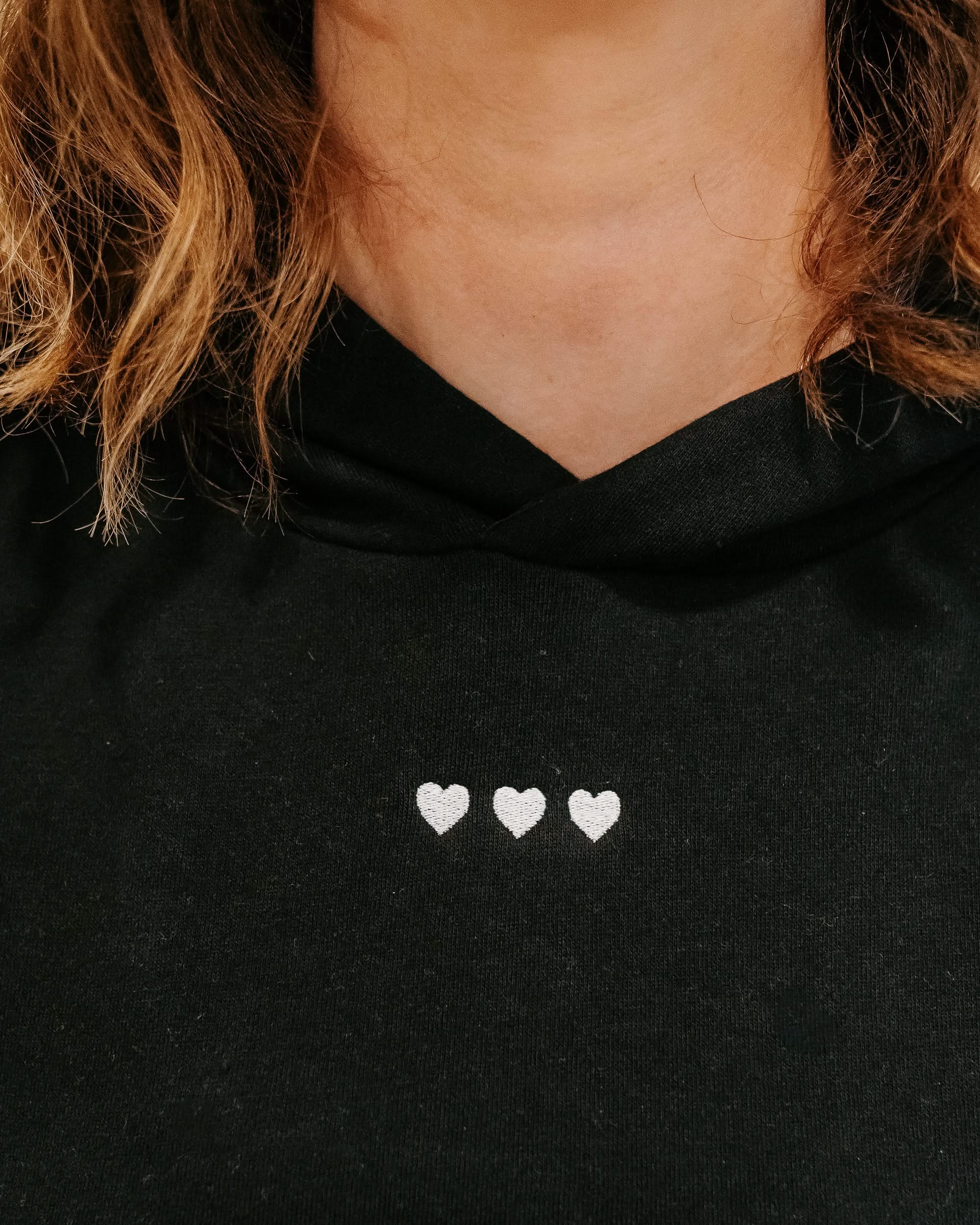 Hoodie chest close up black with white with three embroidered hearts on model - Little Mama Shirt Shop