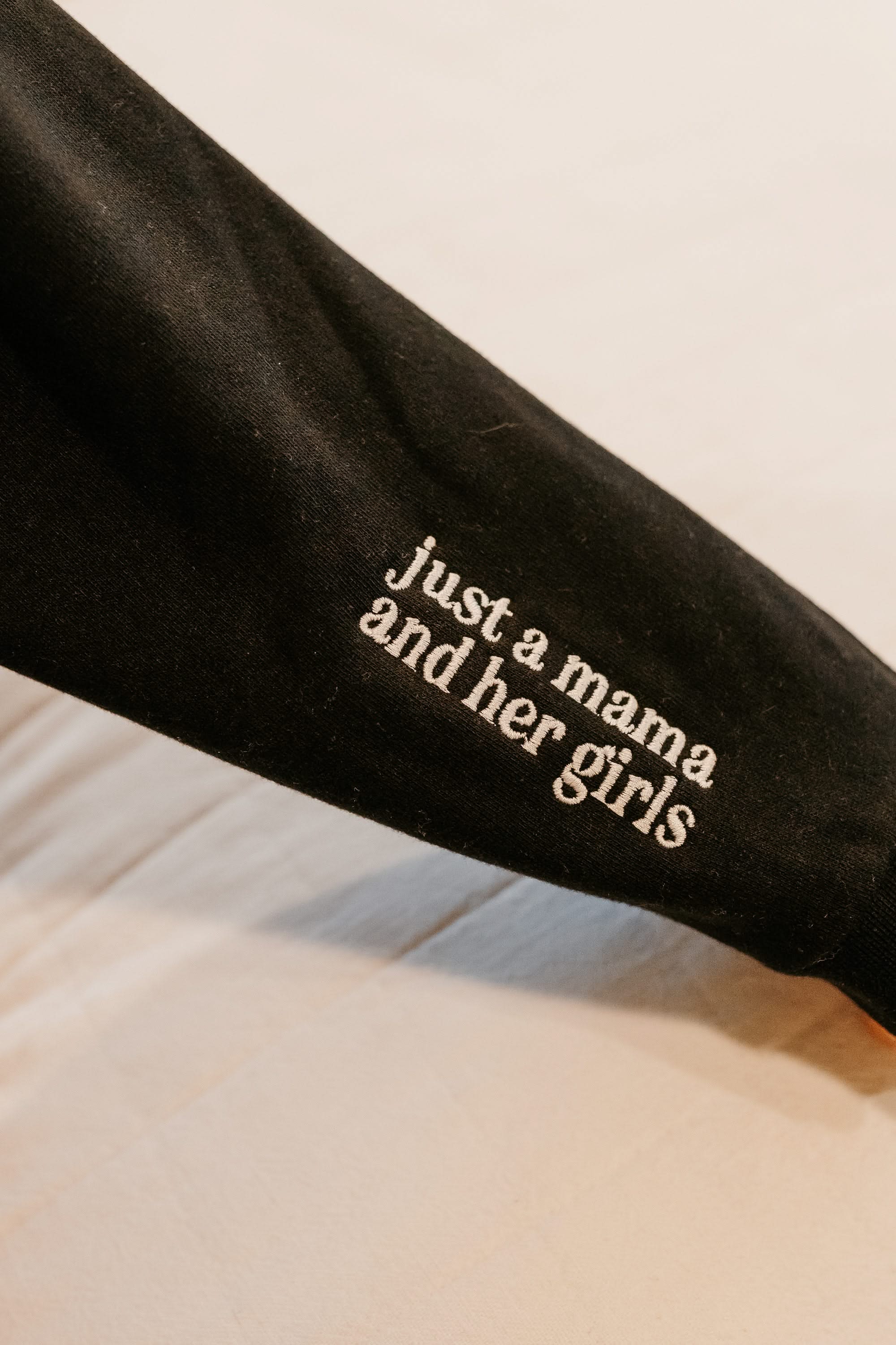 Hoodie sleeve close up black with white  embroidered 'just a mama and her girls' on flat lay - Little Mama Shirt Shop