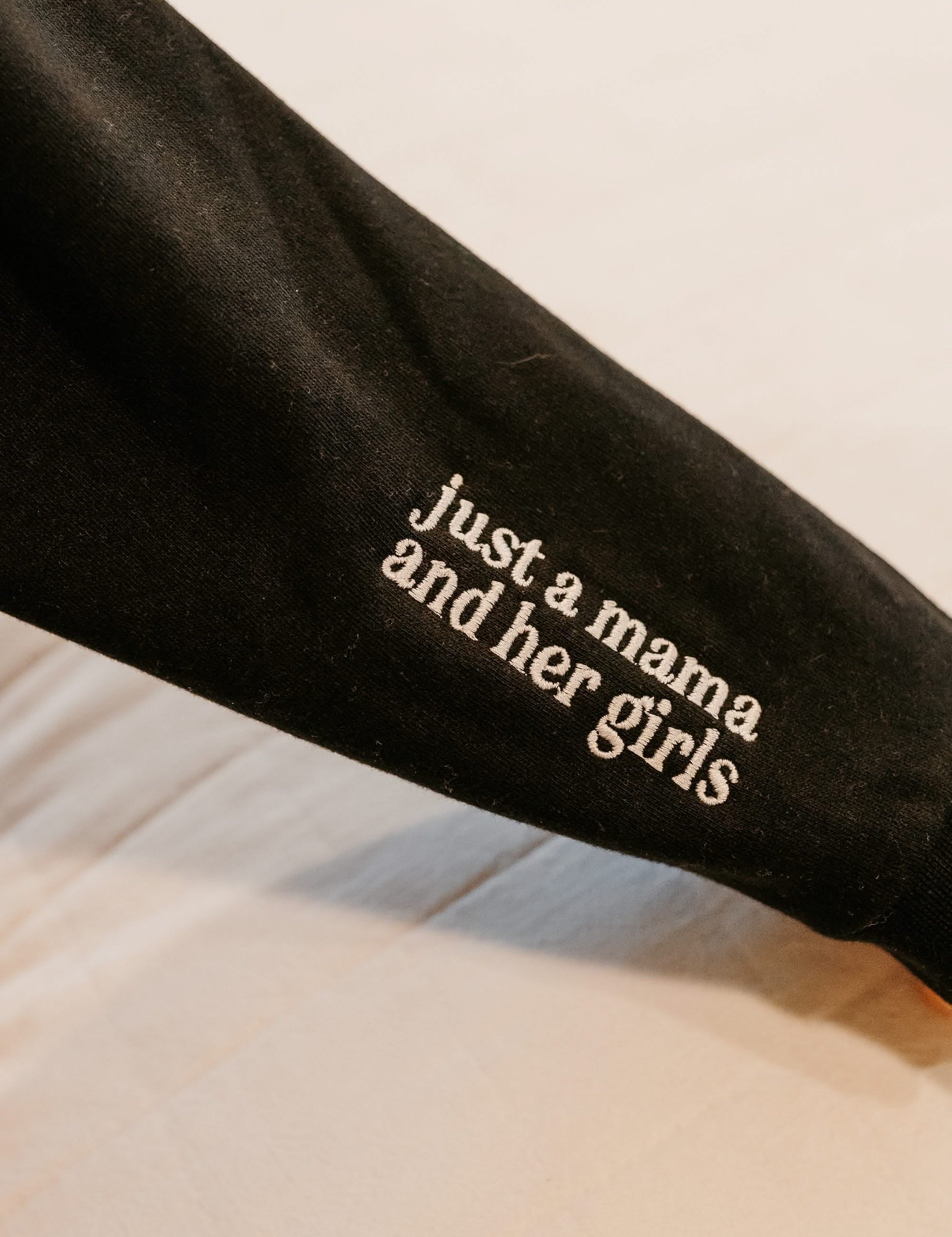Hoodie sleeve close up black with white  embroidered 'just a mama and her girls' on flat lay - Little Mama Shirt Shop