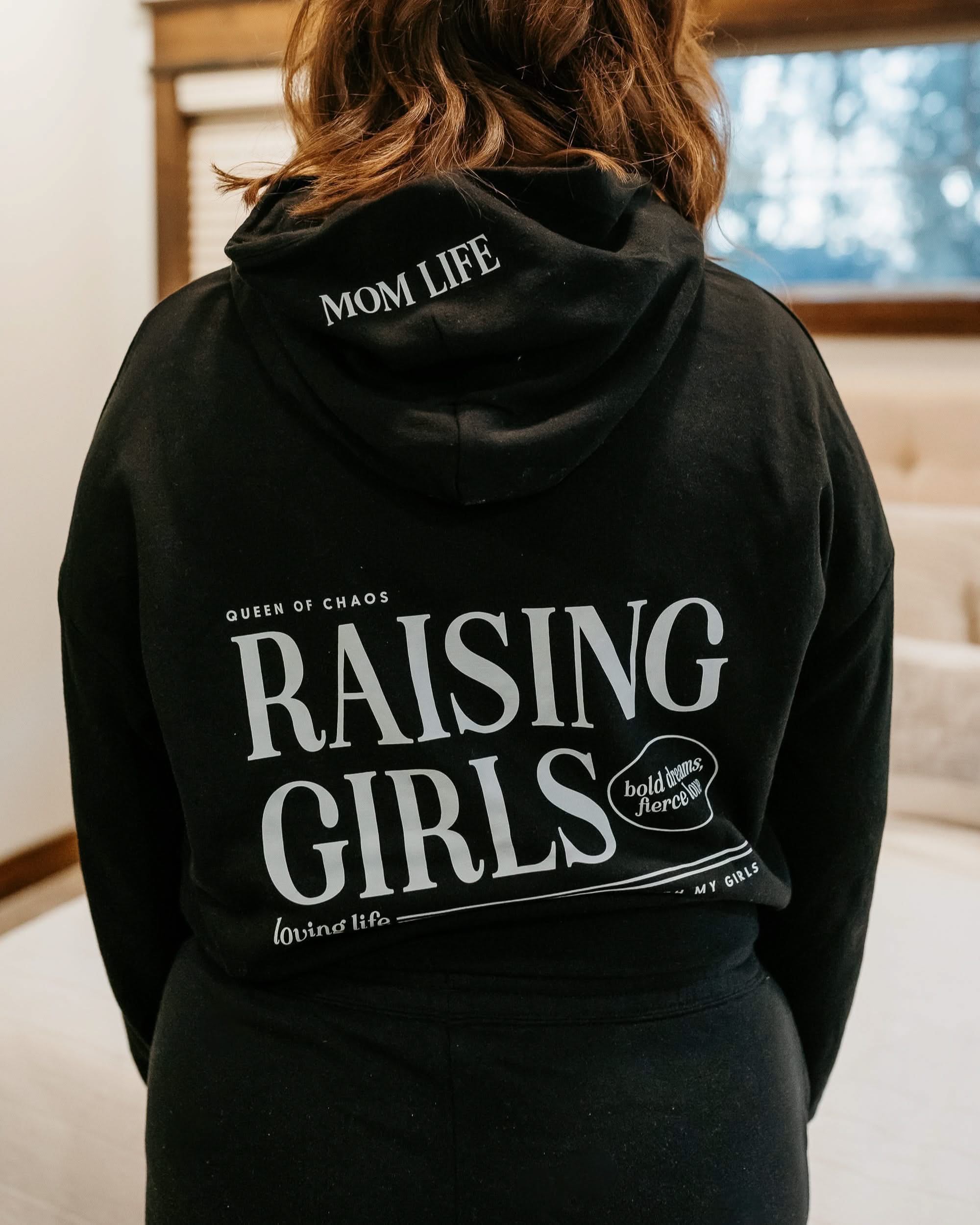 Hoodie in black with white 'Raising Girls' graphic on model - Little Mama Shirt Shop