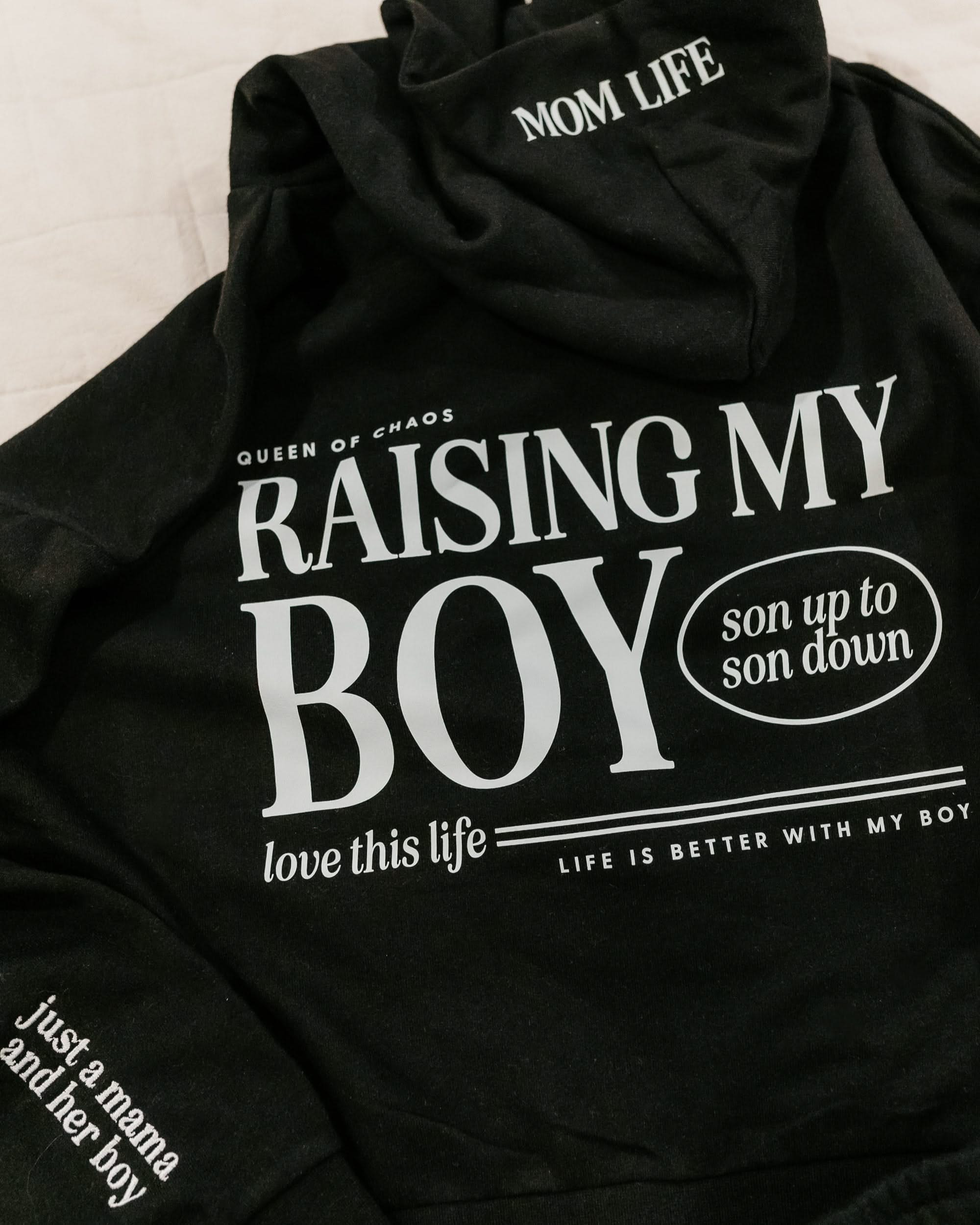 Hoodie in black with white 'Raising My Boy' graphic on flat lay - Little Mama Shirt Shop