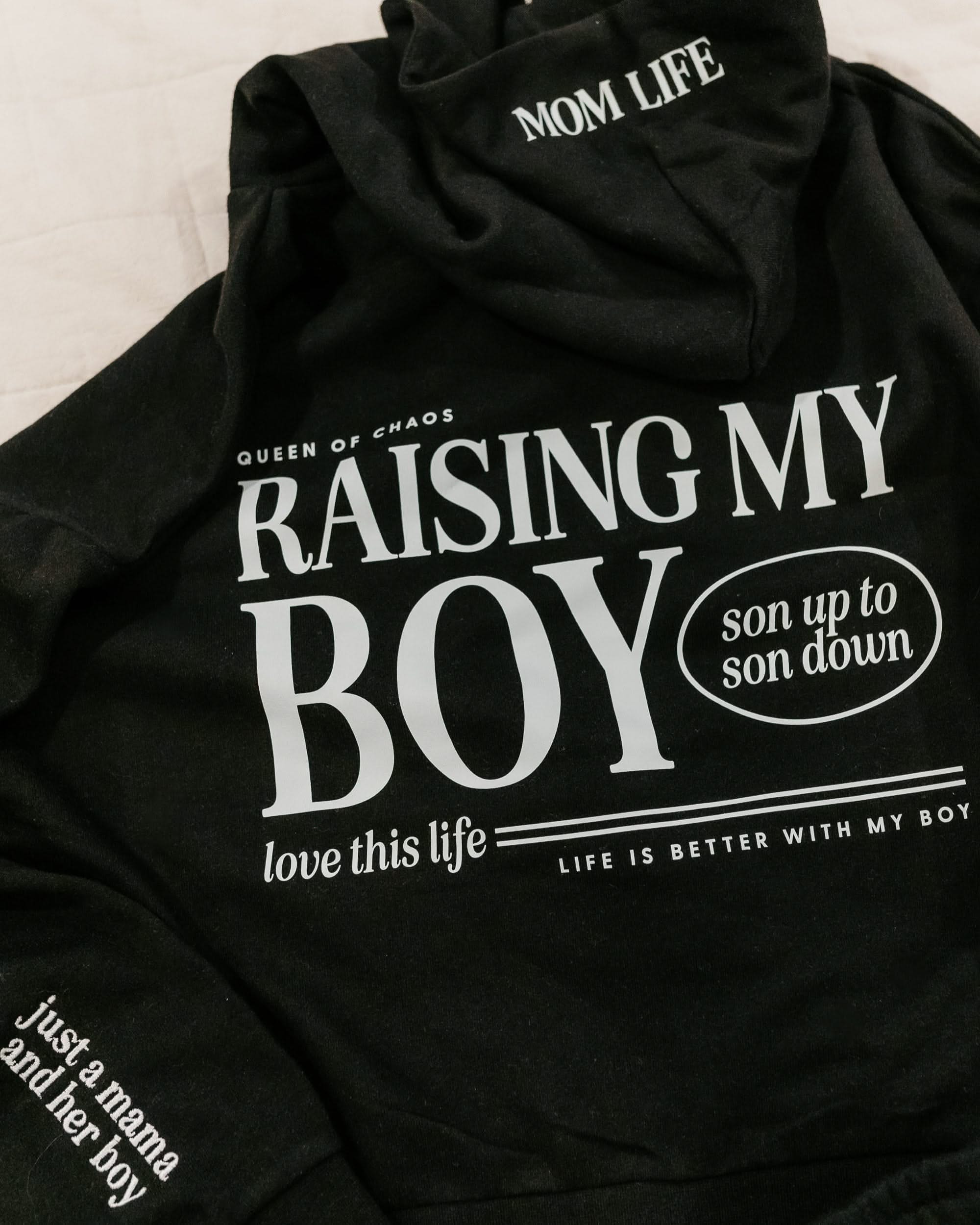 Hoodie in black with white 'Raising My Boy' graphic on flat lay - Little Mama Shirt Shop