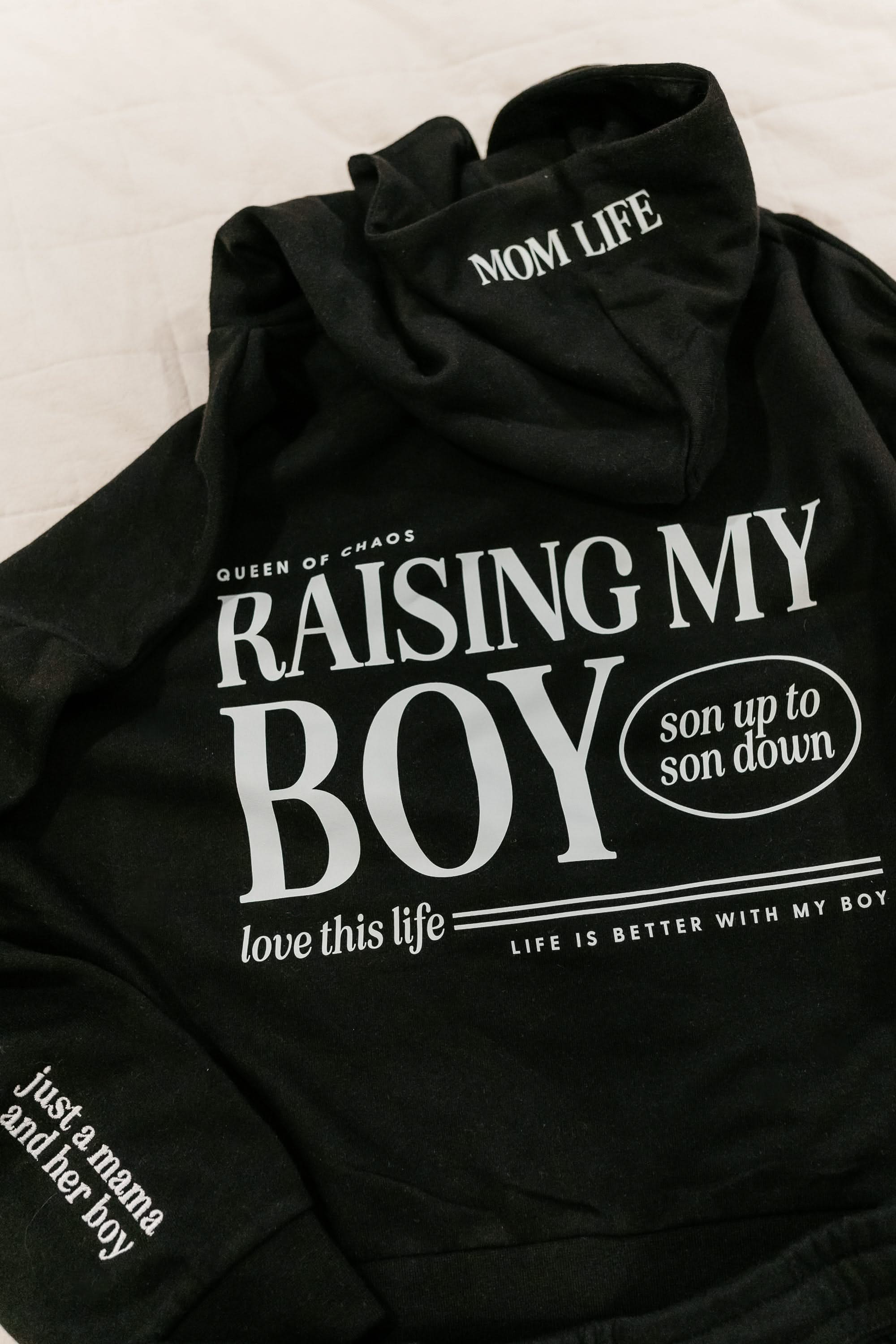 Hoodie in black with white 'Raising My Boy' graphic on flat lay - Little Mama Shirt Shop