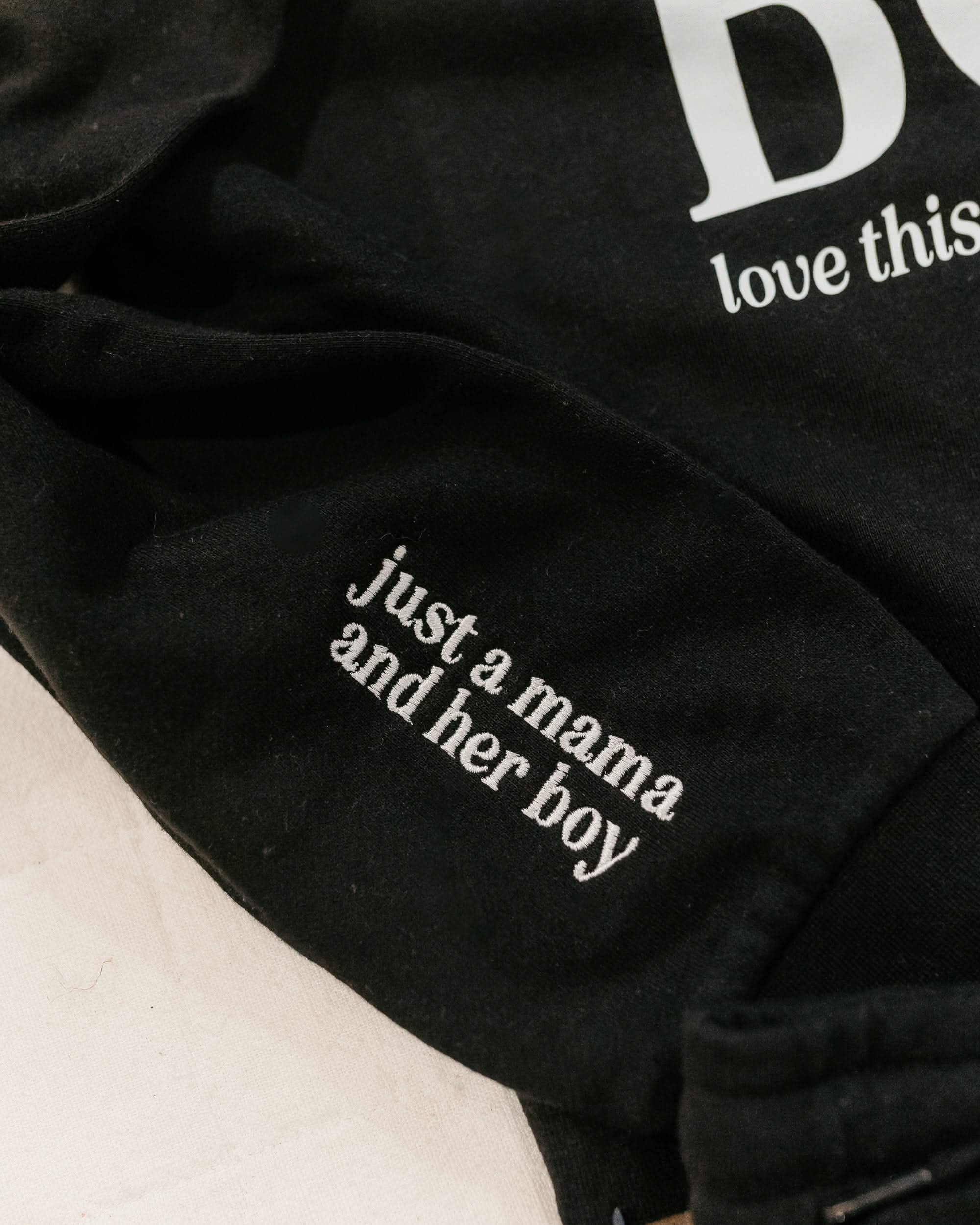 Hoodie sleeve close up black with white  embroidered 'just a mama and her boy' on flat lay - Little Mama Shirt Shop